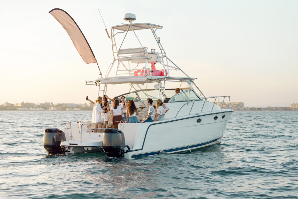 Youth party on vacation at sea. Girlfriends drink champagne and alcohol, have fun, share selfies on a mobile phone, dance on the platform of a catamaran yacht in the sea in the sunlight.