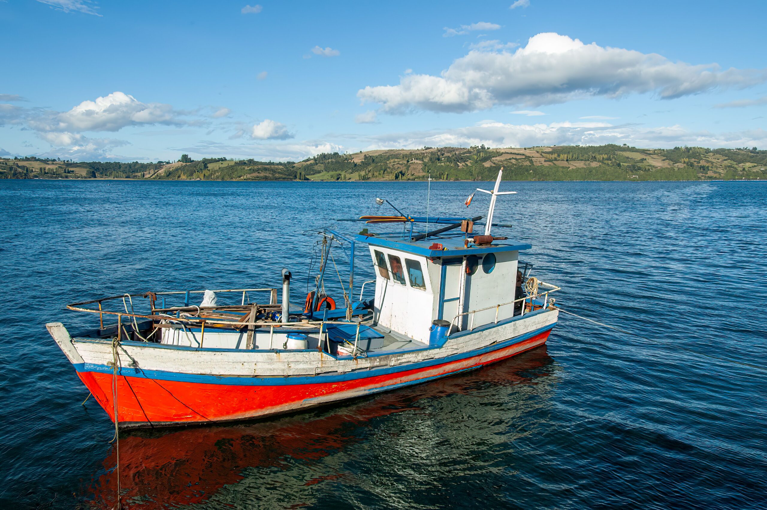 Boat sailing on the water surface in Chiloe Island in Chile, with landscape in the background